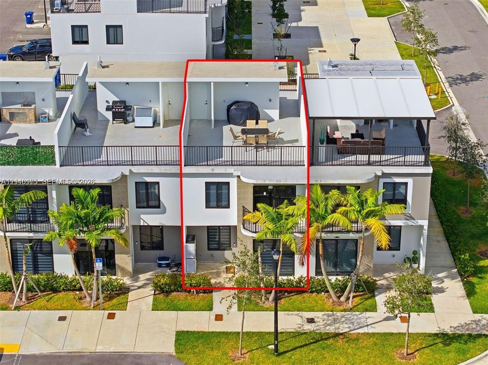 Multi-level townhome featuring a rooftop terrace with metal railings, glass sliding doors, dark-framed windows, and a paved ground-level entry area