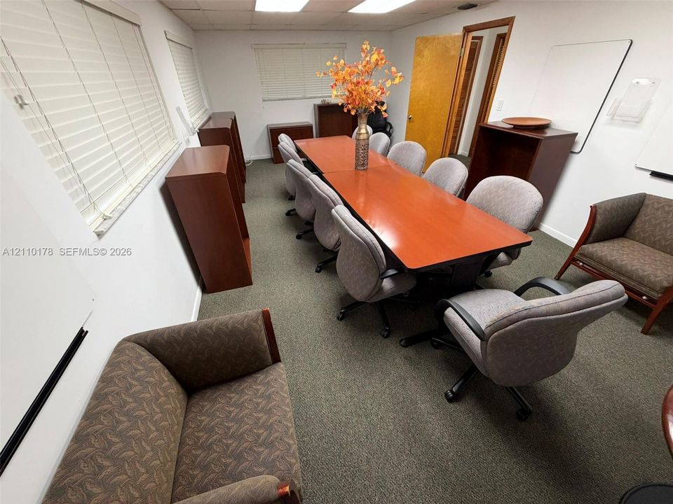 Interior room featuring neutral wall-to-wall carpeting, multiple windows with horizontal blinds, and a suspended drop ceiling