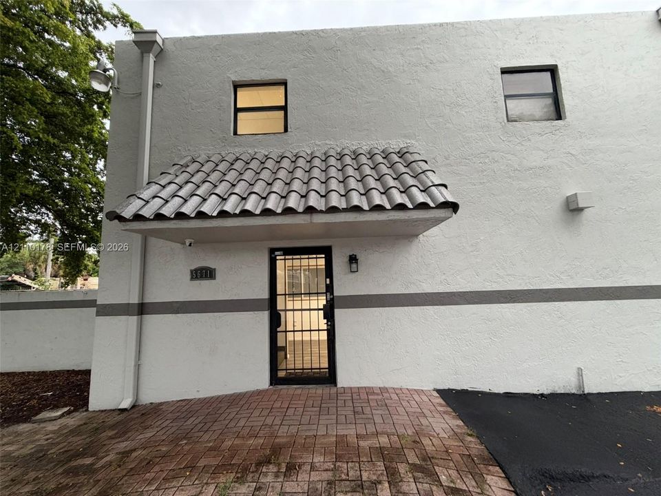 Stucco exterior featuring a decorative tile-roof awning, brick paver entryway, and metal security door