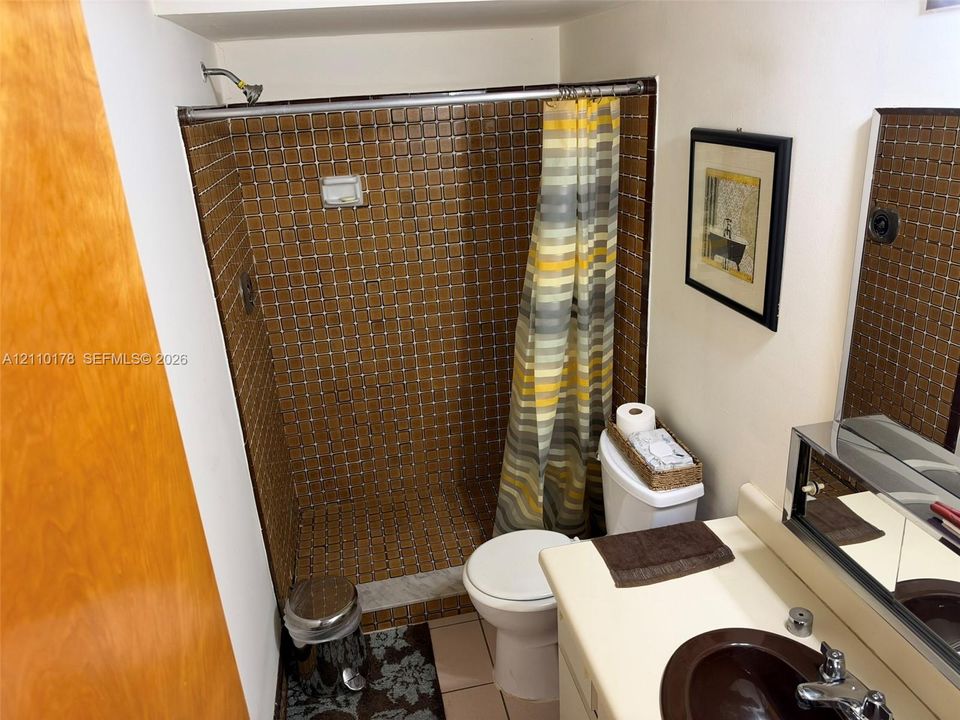 Shower enclosure with square tile surround, vanity featuring a rounded basin, and integrated wall-mounted medicine cabinet