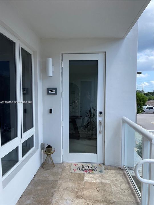 Entryway featuring a full-length glass-panel door, natural stone flooring, and a glass-paneled railing