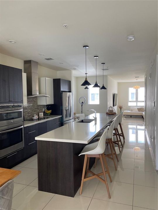 Kitchen featuring an expansive stone-surface island, stainless steel wall-mounted oven, built-in flat-panel cabinetry, stone-tiled backsplash, and recessed lighting