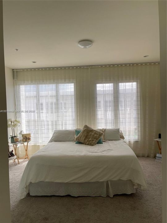 Expansive windows featuring floor-to-ceiling sheer drapery, plush carpeting, and recessed ceiling lighting