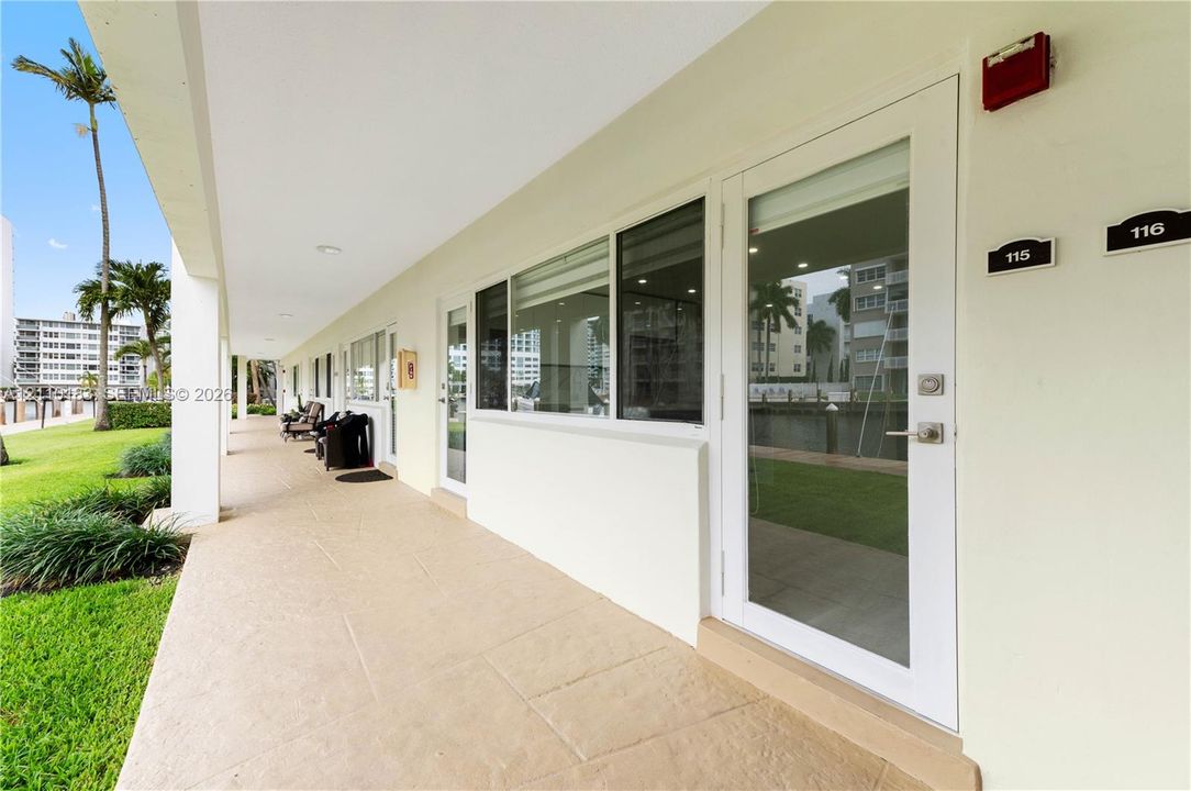 Covered walkway featuring paved flooring, white-framed glass-paneled exterior doors, and large windows with horizontal blinds
