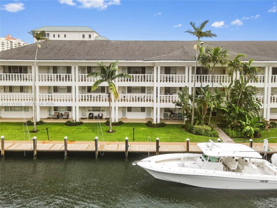 Multi-level residential exterior featuring wrap-around balconies with balustrade railings, private wooden dock, and manicured lawn