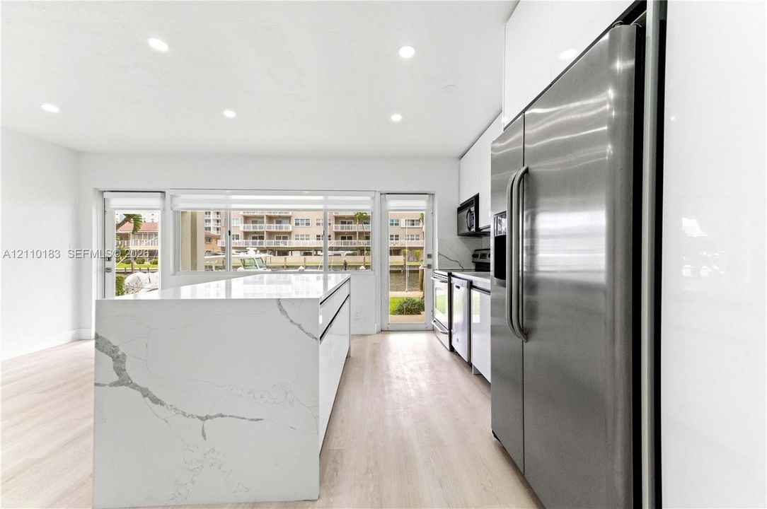 Kitchen featuring a waterfall-edge island with stone-finish countertop, high-gloss white cabinetry, stainless steel side-by-side refrigerator, recessed lighting, and wood-finish flooring