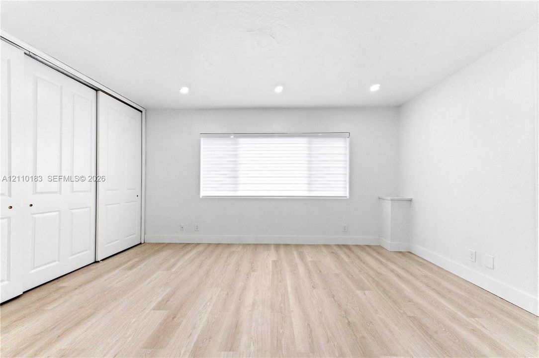 Neutral-toned wood-finish flooring, recessed lighting, and a large horizontal window featuring interior blinds, complemented by white dual-panel sliding closet doors