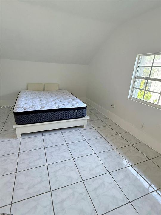 Light-filled room featuring white-toned tile flooring, angled ceiling, and a multi-pane grid window
