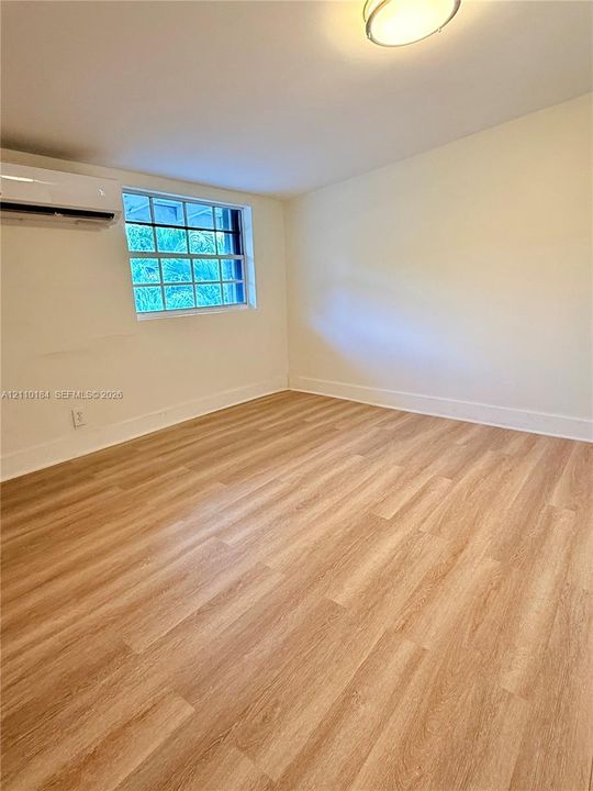 Room featuring wood-finish flooring, a wall-mounted ductless air conditioning unit, a multi-pane window, and a flush-mount ceiling light fixture