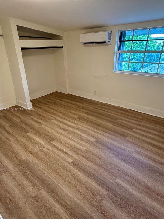 Interior space featuring wood-finish flooring, a wall-mounted ductless mini-split system, a multi-pane window, and a built-in closet with hanging rods