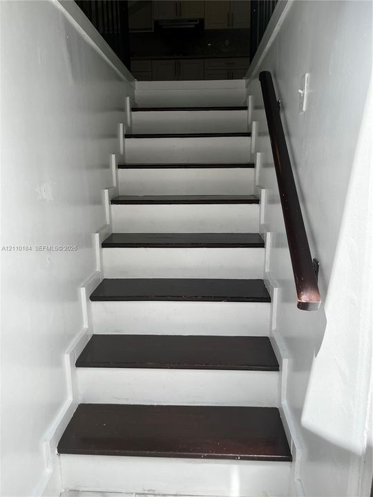 Staircase featuring dark-stained wood treads, white risers, and a dark-stained wood handrail