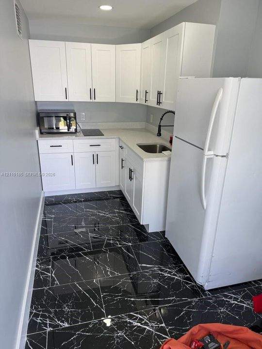 Kitchen featuring white shaker-style cabinetry, quartz countertops, high-contrast dark stone-finish flooring, and a matte black pull-down faucet