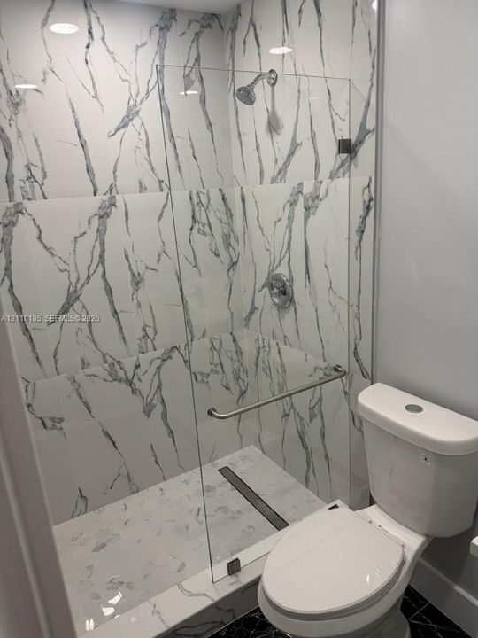 Walk-in shower featuring floor-to-ceiling veined tile, frameless glass enclosure, polished metal hardware, and linear drain