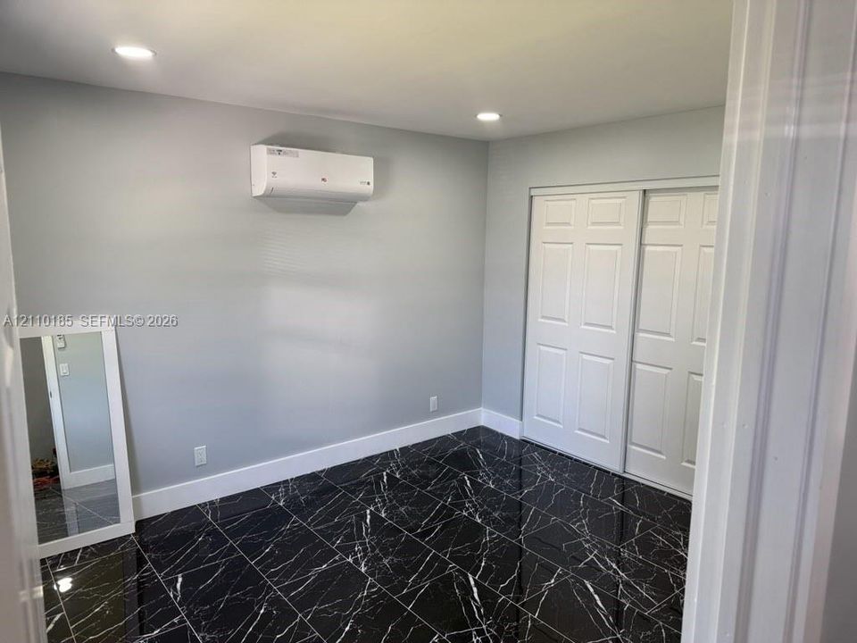 Interior space featuring high-gloss dark stone-finish tile flooring, a wall-mounted ductless mini-split climate control system, recessed ceiling lighting, and a white sliding-panel closet