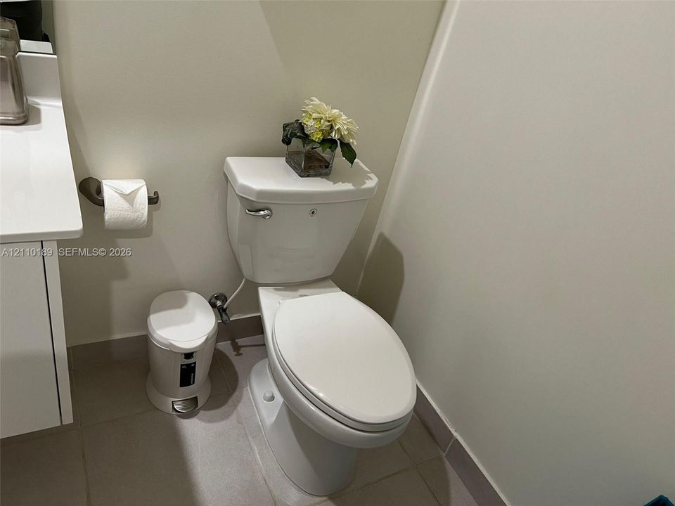 White bathroom featuring a solid-surface countertop with a vanity cabinet, chrome-finished hardware, and ceramic tile flooring
