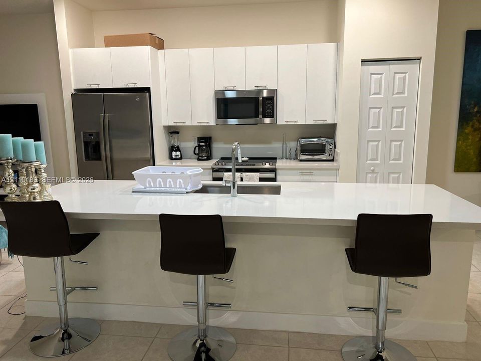 Kitchen featuring flat-panel white cabinetry, a large quartz-topped center island with an integrated stainless steel sink, and stainless steel appliances