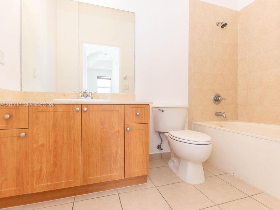 Bathroom featuring wood-finish cabinetry, a neutral stone countertop with an integrated basin, a wall-to-wall vanity mirror, ceramic tile flooring, and a tub-shower combination with tiled surround