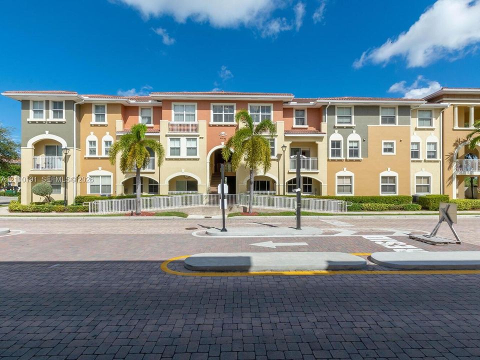 Multi-story Mediterranean-style exterior featuring stucco facade, arched architectural detailing, balcony enclosures, and decorative tile roof elements