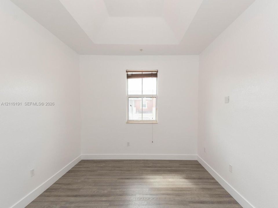 Room featuring tray ceilings, wood-finish flooring, and a central window with integrated blinds