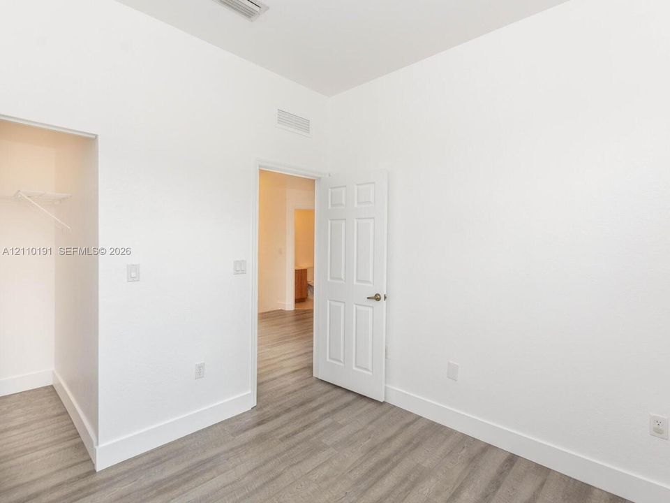 Neutral interior featuring wood-finish flooring, a six-panel door with a metallic knob, and an open-access closet with a built-in wire shelf