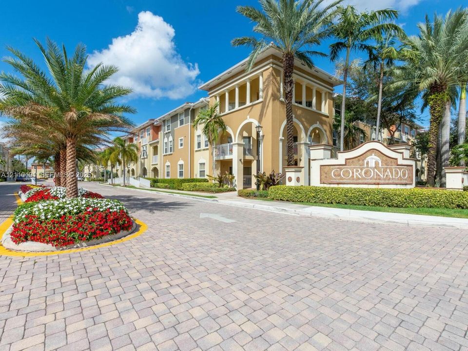 Stucco exterior featuring arched architectural detailing, paved stone driveway, and established tropical landscaping
