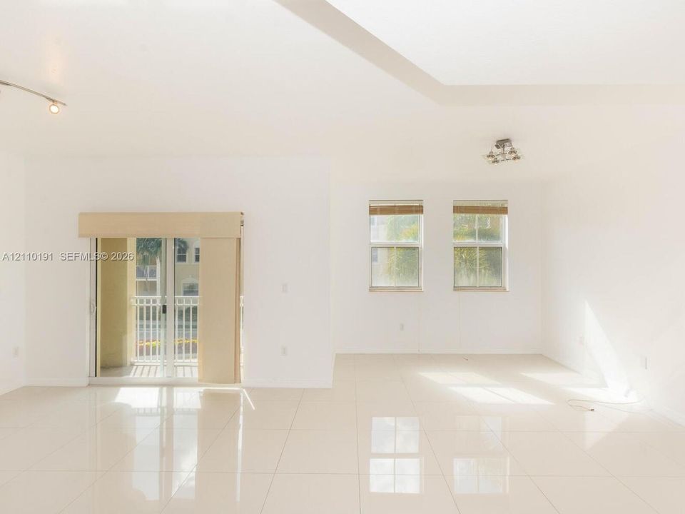 Open floor plan featuring oversized tile flooring, recessed tray ceiling detailing, sliding glass doors to a private balcony, and dual-pane windows