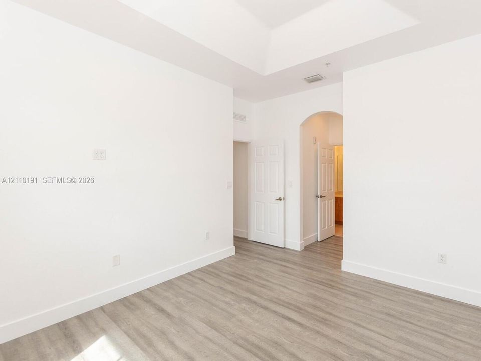 Interior space featuring wood-finish flooring, a tray ceiling, and an arched doorway leading to a secondary room