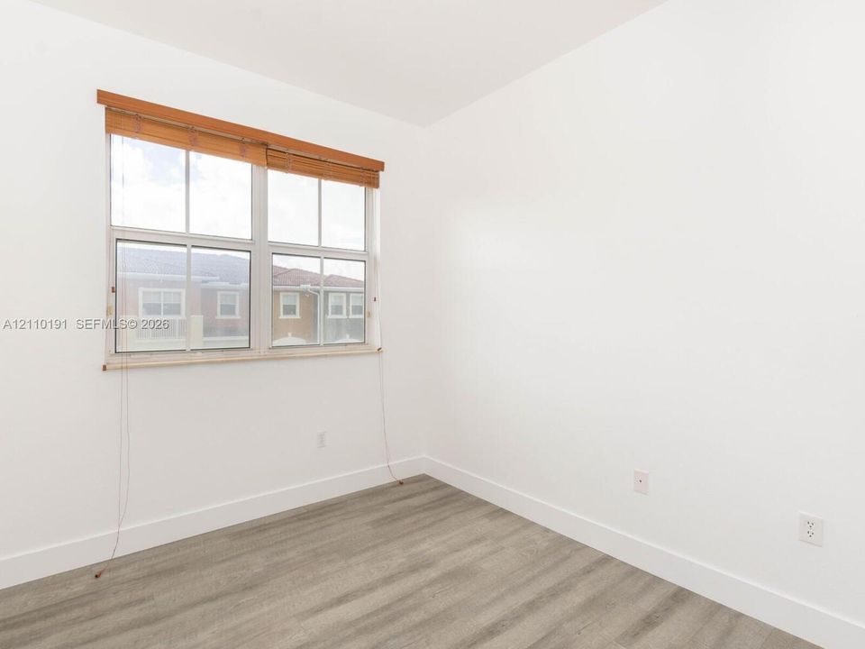 Neutral-toned interior space featuring wood-finish flooring, crisp white walls, and a multi-pane window with wood-slat blinds