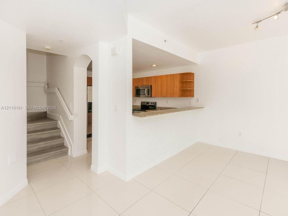 Kitchen featuring flat-panel wood cabinetry, stone-finish countertops, and stainless steel built-in appliances, complemented by a stone-tile floor and a structural arched entryway