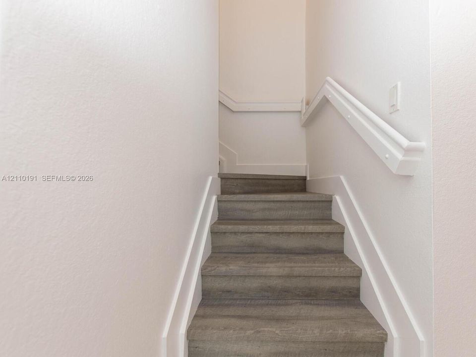 Staircase featuring wood-finish treads, crisp white trim, and a matching handrail