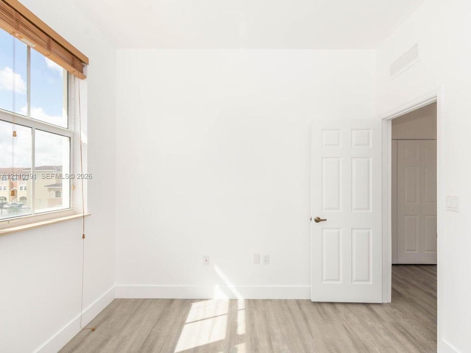 Wood-finish flooring, multi-pane window with wood-trim framing, six-panel interior door, and smooth-finish walls