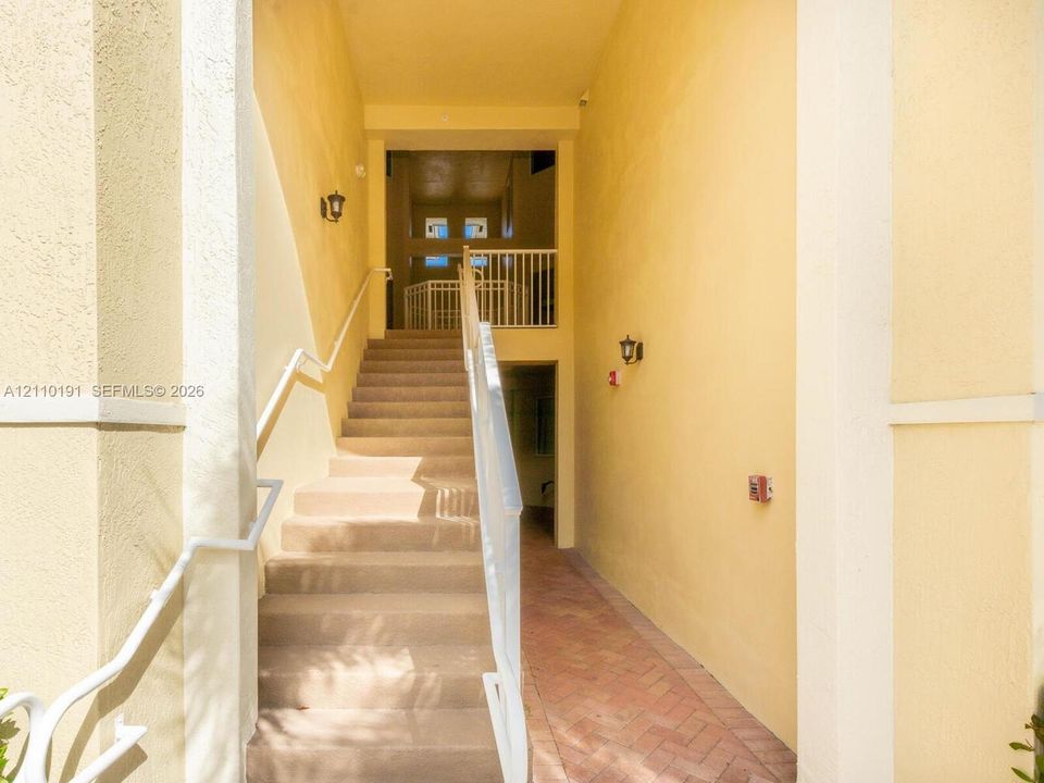 Exterior staircase featuring stucco walls, a herringbone-pattern brick pathway, and white metal railings