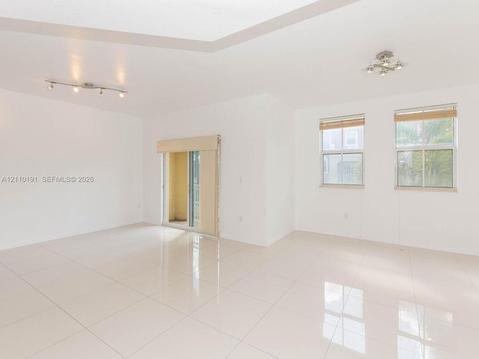Open-concept space featuring polished ceramic tile flooring, recessed tray ceiling, multi-light track fixtures, and dual-pane windows