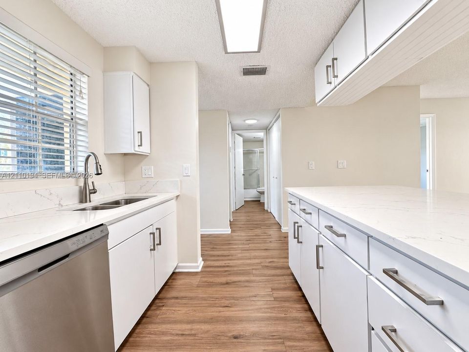 Kitchen featuring white shaker-style cabinetry, quartz countertops with veining, stainless steel undermount sink with gooseneck faucet, stainless steel dishwasher, and wood-finish flooring