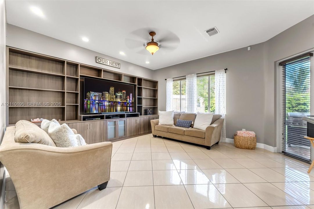 Living area featuring large-format tile flooring, recessed lighting, a ceiling fan, and floor-to-ceiling custom built-in cabinetry with integrated shelving