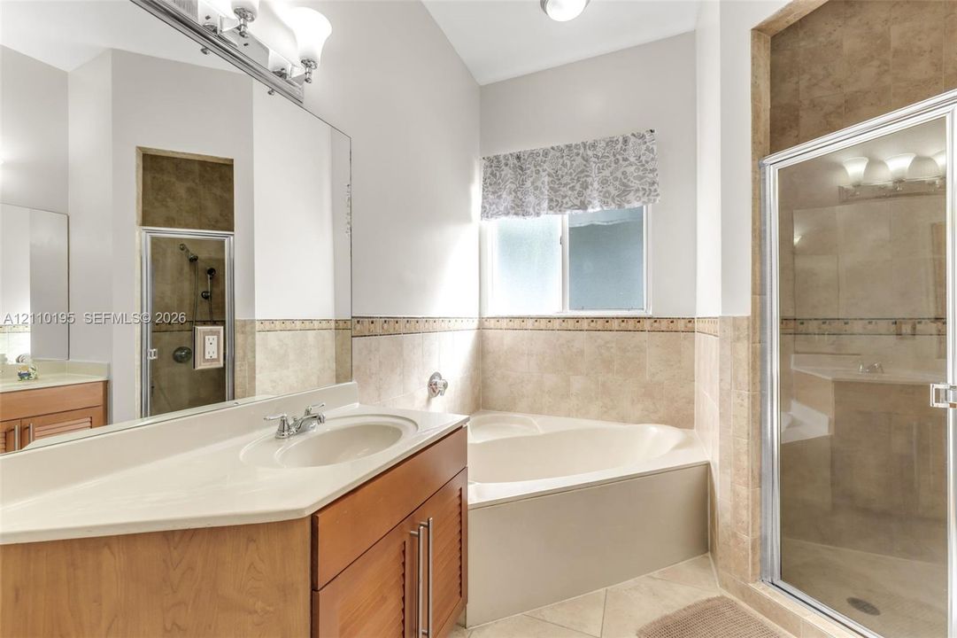 Bathroom featuring wood-finish cabinetry, a drop-in soaking tub, a separate glass-enclosed shower, neutral tile backsplash, and a large wall-mounted mirror
