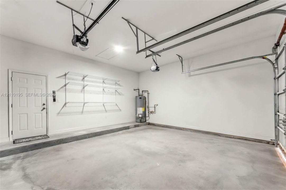 Attached garage featuring a concrete floor, finished interior walls, built-in wire wall shelving, and an automatic door opener