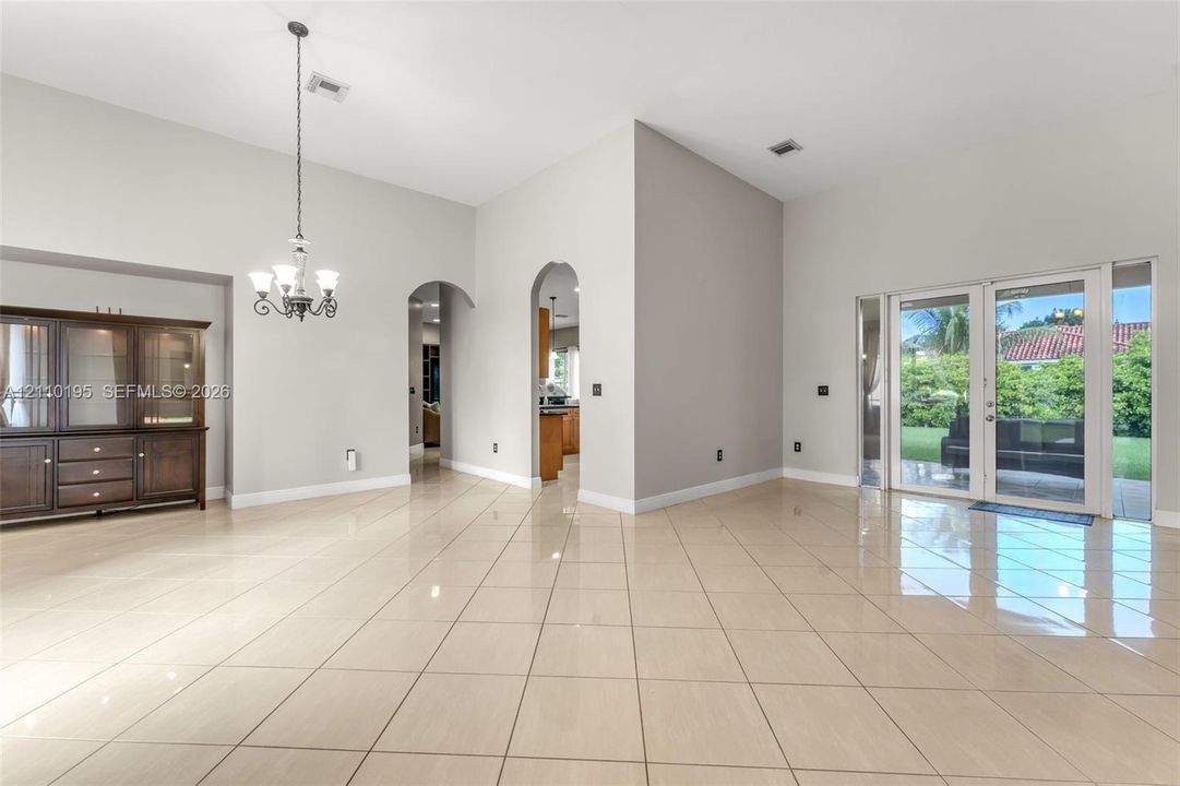 High-ceilinged room featuring large-format tile flooring, arched doorways, a classic multi-light chandelier, and glass patio doors
