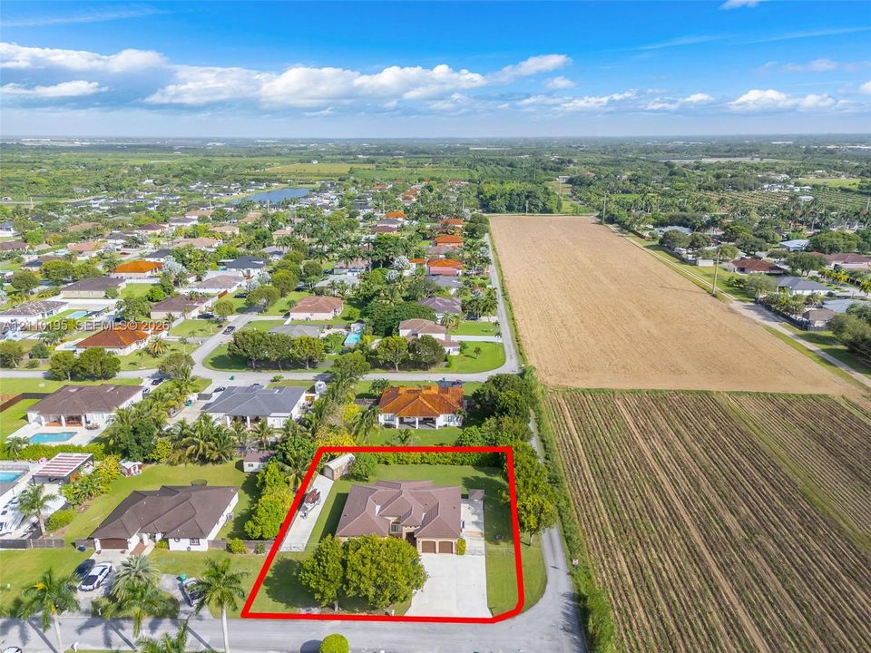 Aerial perspective of a detached residential property featuring a hipped roof, multi-car garage, concrete driveway, and mature landscaping within a bordered lot