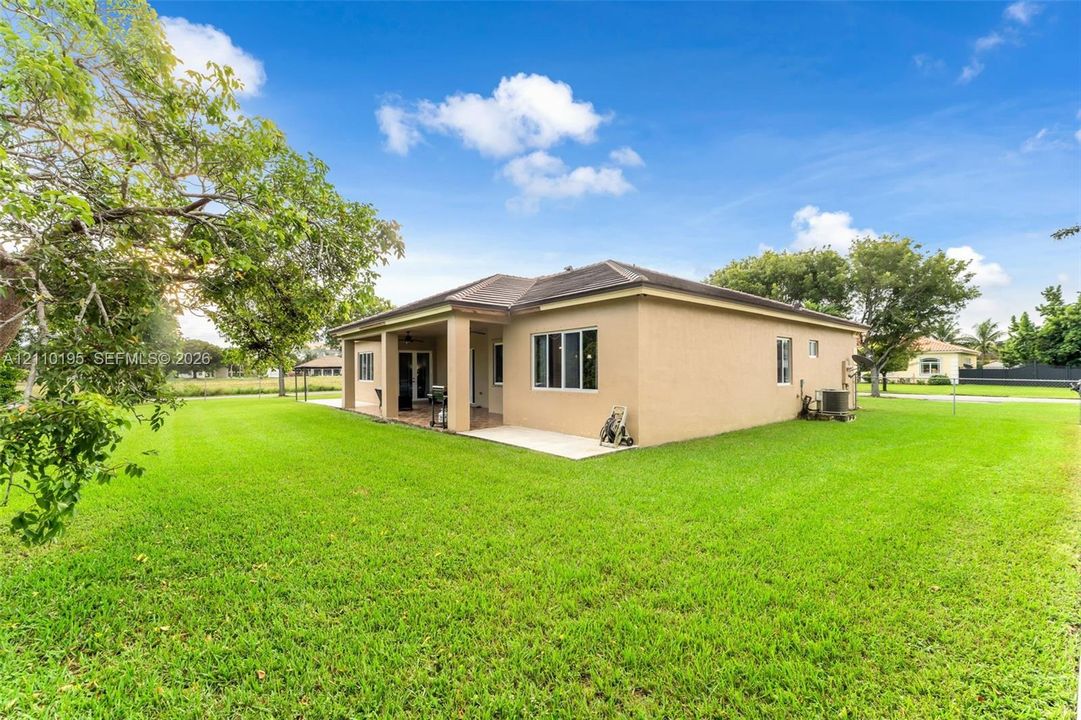 Stucco exterior featuring a hipped roof, covered rear patio, and expansive manicured lawn