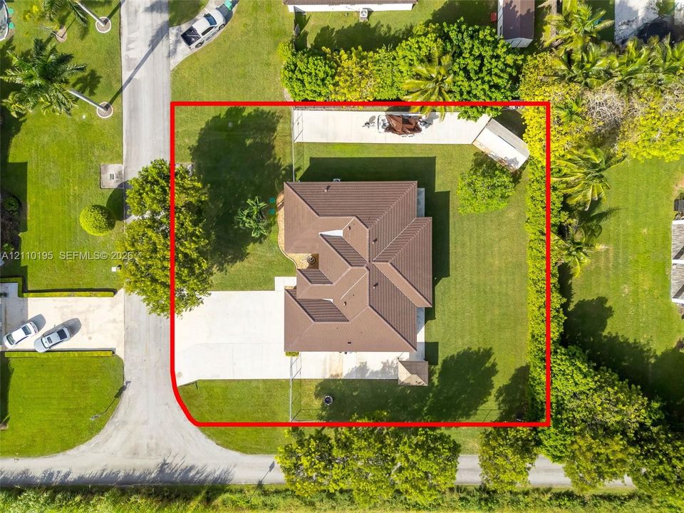 Corner lot featuring a multi-hipped roof, expansive lawn, concrete driveway, and established perimeter hedging