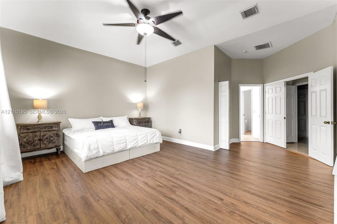 Spacious room featuring a vaulted ceiling, wood-finish flooring, ceiling fan with integrated lighting, and multi-panel interior doors