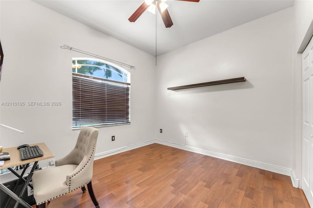 Wood-finish flooring, arched window with horizontal blinds, ceiling fan, and built-in wall-mounted shelf