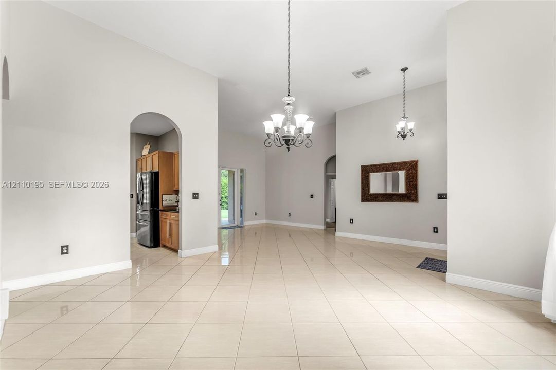 Open-concept interior featuring light-toned tile flooring, vaulted ceilings, dual decorative chandeliers, and arched architectural entryways