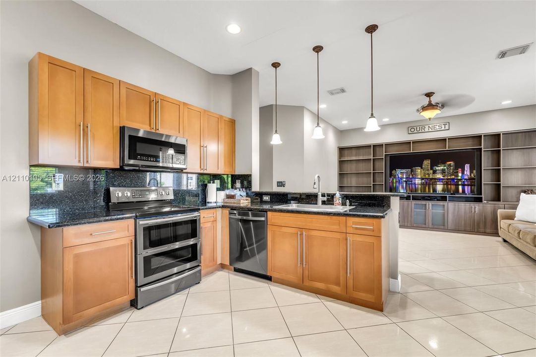Kitchen featuring light-finish cabinetry, dark stone countertops, stainless steel appliances, pendant lighting, and built-in shelving