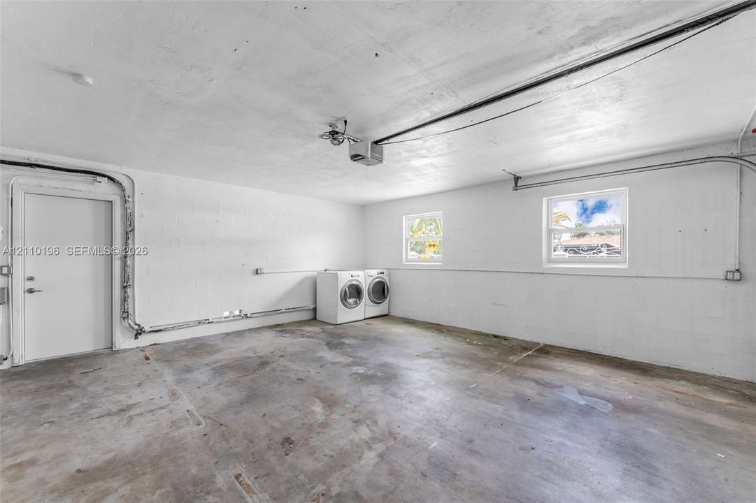Garage space featuring concrete flooring, painted block walls, two windows, and an exterior access door
