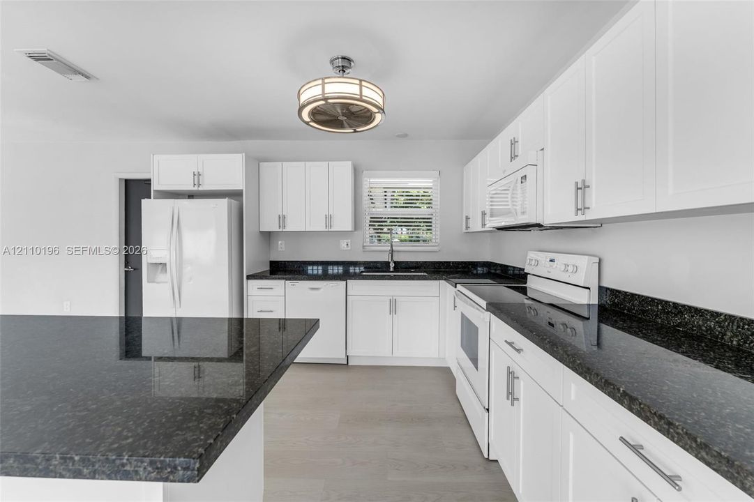 Kitchen featuring white shaker-style cabinetry, dark stone countertops, an integrated island, wood-finish flooring, and a drum-style ceiling light fixture