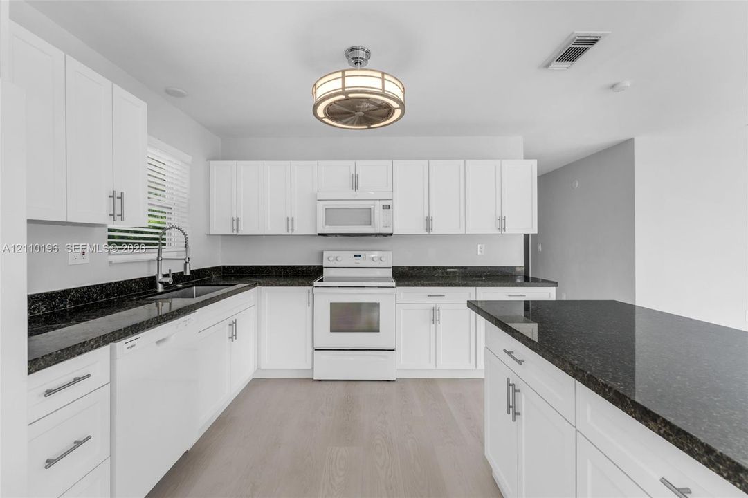 Kitchen featuring white shaker-style cabinetry, dark stone countertops, an integrated island, wood-finish flooring, and a circular drum-style light fixture