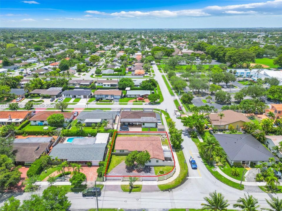Aerial perspective featuring a corner lot, paved driveway, sprawling lawn with mature landscaping, and a terracotta-tiled roof