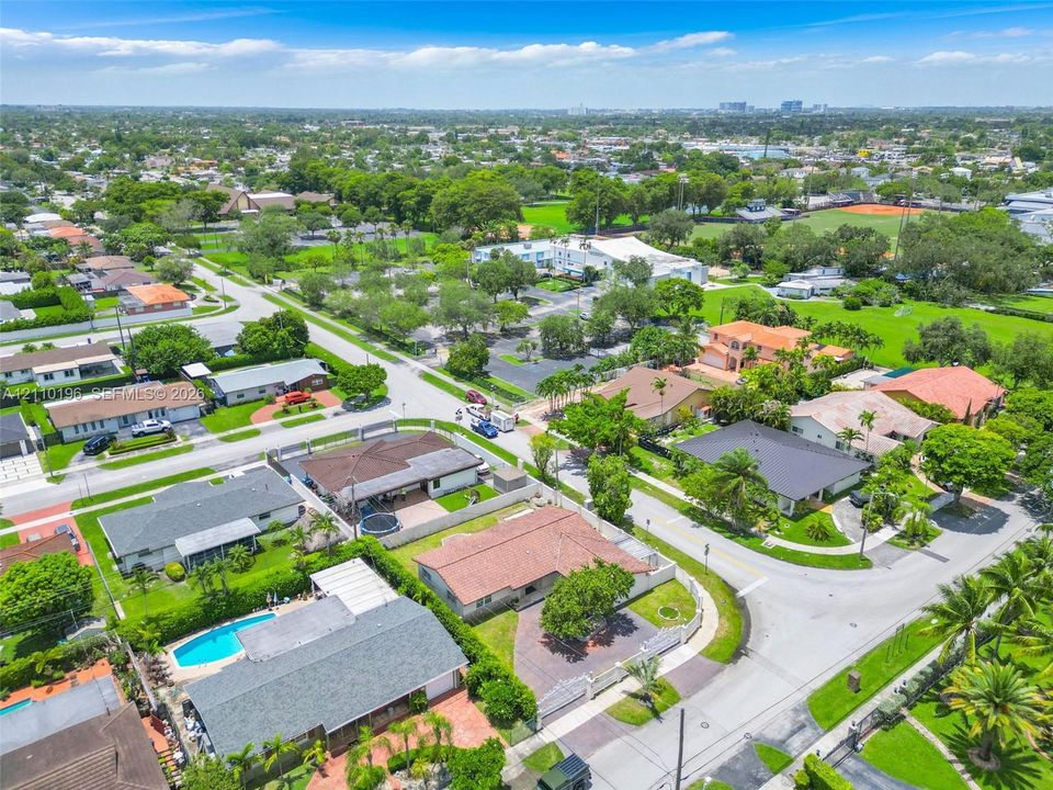 Aerial perspective of a corner lot featuring a tile roof, paved driveway, enclosed yard, and swimming pool